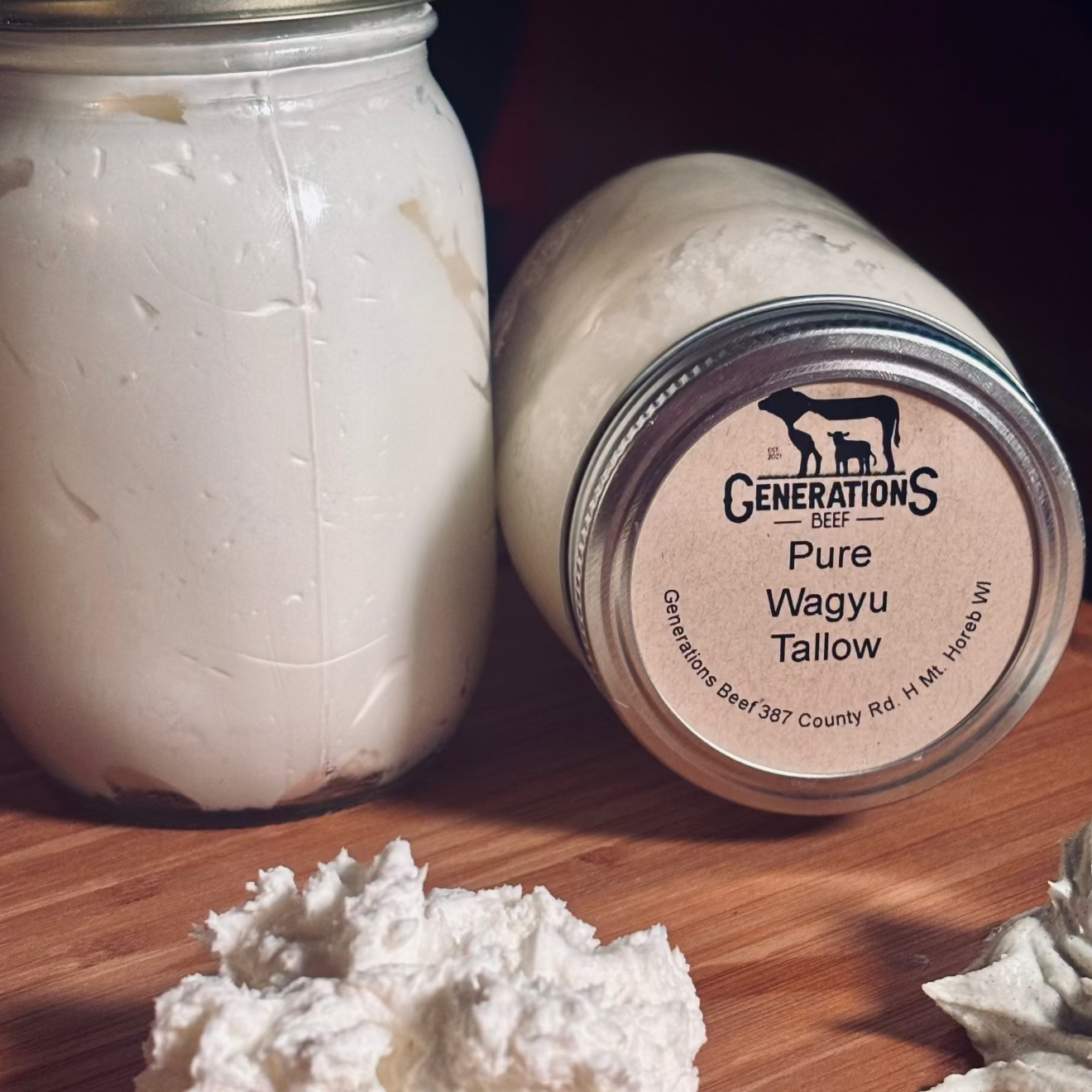 Two jars of 'Generations Beef' Pure Wagyu Tallow on a wooden surface with some tallow outside the jars.