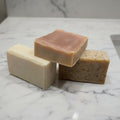 Three bars of soap stacked on a textured surface with a dark background